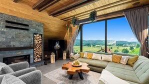 Un salon moderne avec une cheminée en pierre, une grande fenêtre donnant sur la campagne et un coin salon confortable.