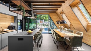 Une cuisine moderne dotée d’un îlot central, d’un coin repas avec une grande table et des chaises, et offrant une vue sur l’extérieur grâce à de grandes fenêtres.