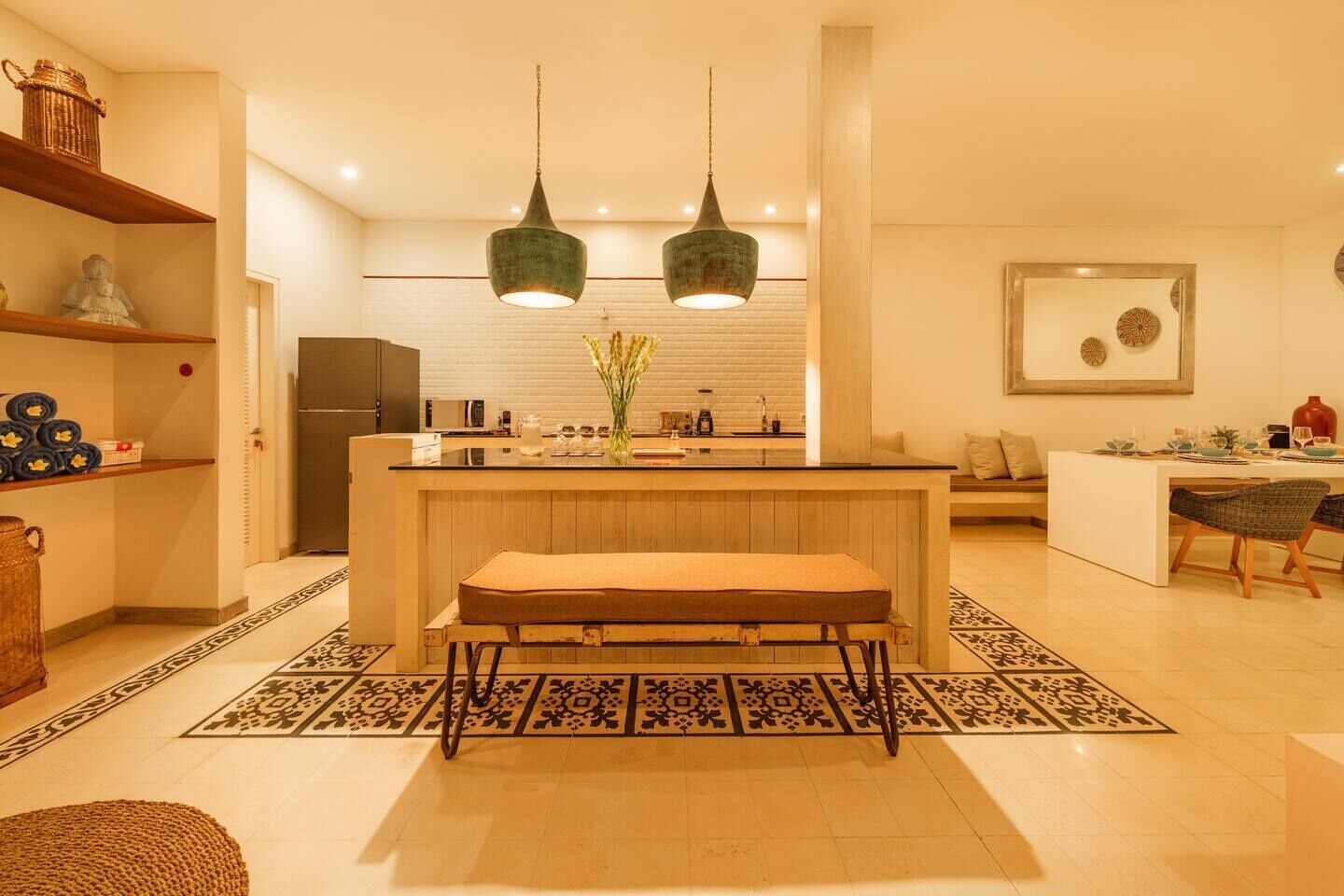 A modern kitchen with a central island, two pendant lights, and a dining area with a bench and chairs.