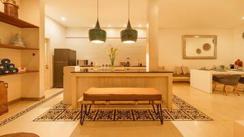 A modern kitchen with a central island, two pendant lights, and a dining area with a bench and chairs.