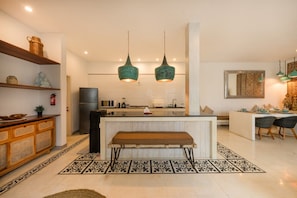 A modern kitchen with a central island, pendant lights, and a dining area with chairs.