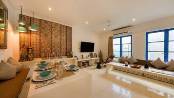 A modern living room with a dining area, large windows, and a flat-screen TV.