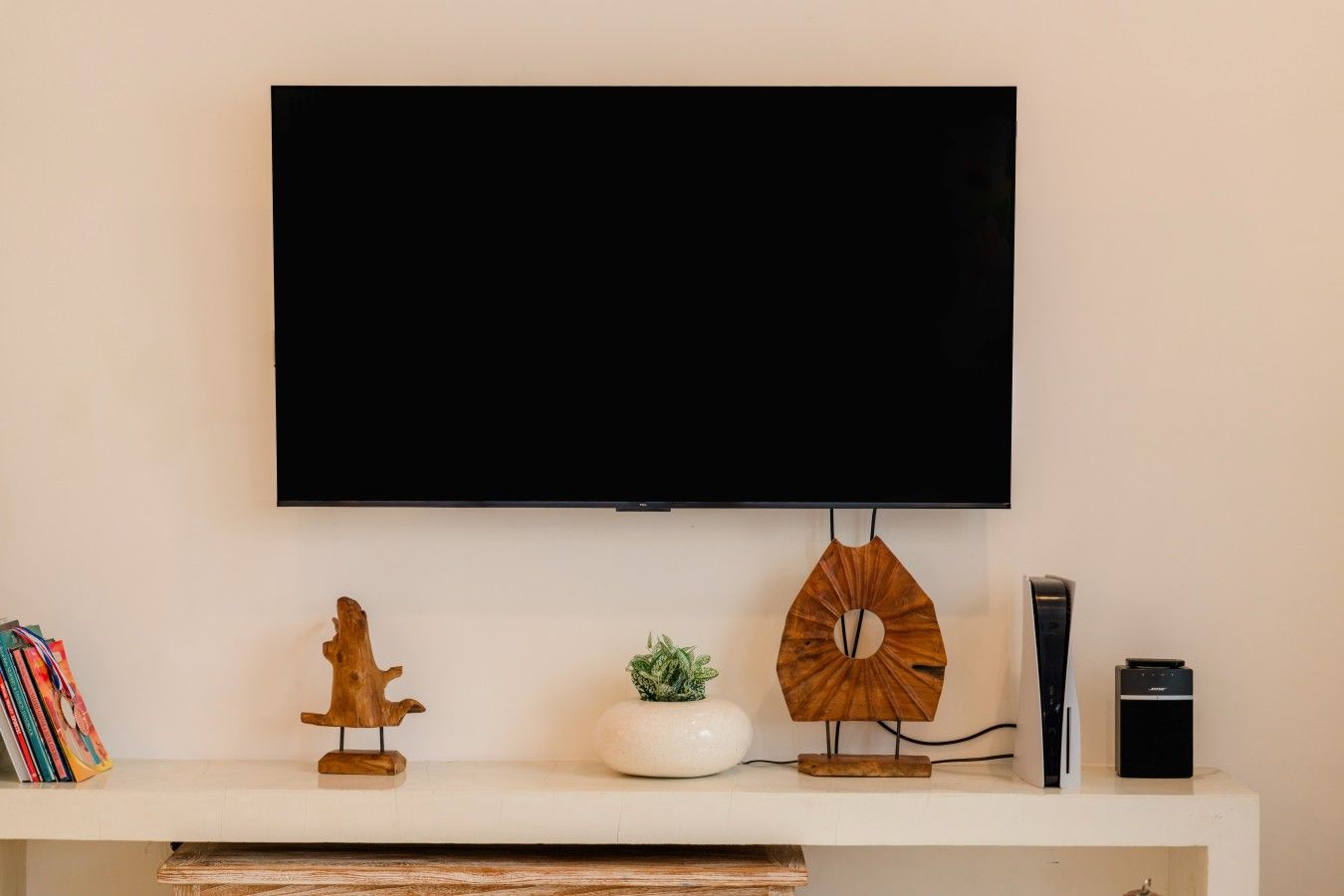 Een flatscreen televisie bevestigd aan een muur, boven een witte console met decoratieve objecten en een speaker.