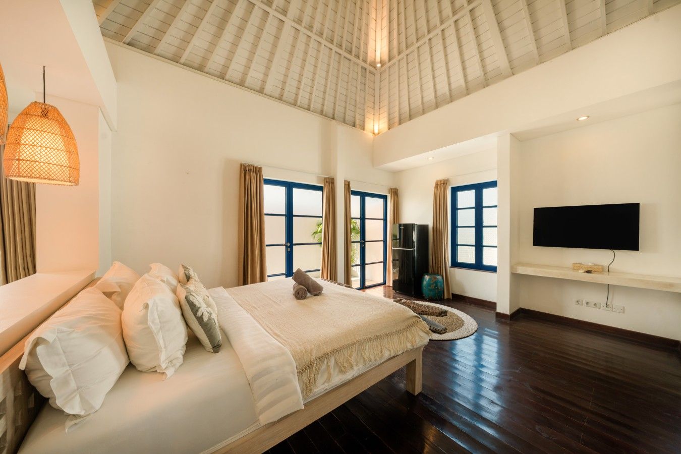 A spacious bedroom with a large bed, a television mounted on the wall, and a view of the outdoors through the windows.