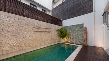 Une piscine avec des murs en pierre, une terrasse en bois et une plante en pot.