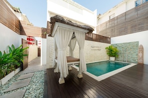 A private pool area with a wooden deck, a stone wall, and a canopy bed.