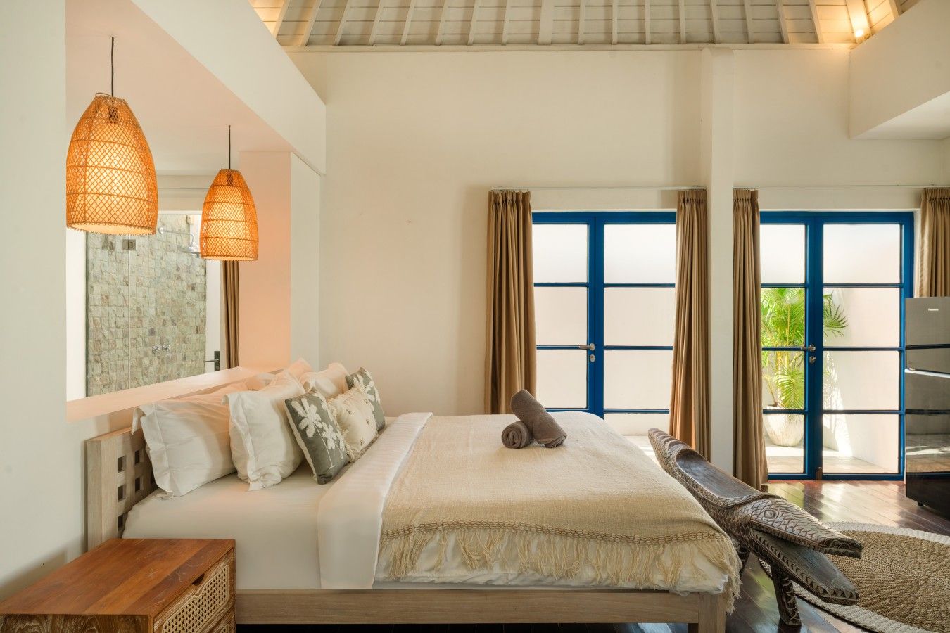 Ein Schlafzimmer mit einem Bett, zwei Pendelleuchten, einem großen Fenster mit Vorhängen und Blick auf Grünfläche.