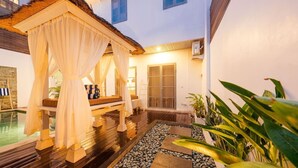 Un área de estar exterior acogedora, con un banco de madera y un toldo, piscina y un sendero de piedra.