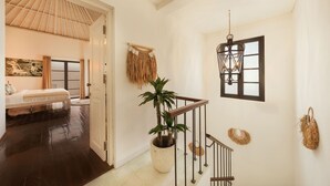 Habitación de hotel con cama, planta en maceta, escalera y farol en la pared.