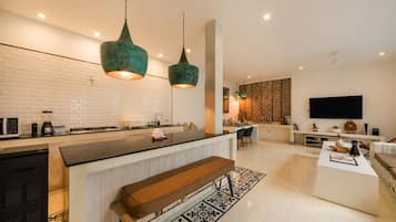 Une cuisine moderne dotée d’un îlot central, d’un éclairage suspendu et d’un téléviseur à écran plat dans un espace de vie agrémenté d’un tapis à motifs.