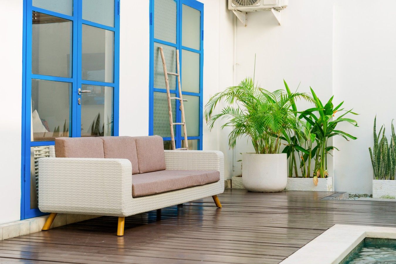 Un espace de détente extérieur moderne, avec un canapé confortable, une échelle en bois et des plantes en pot.