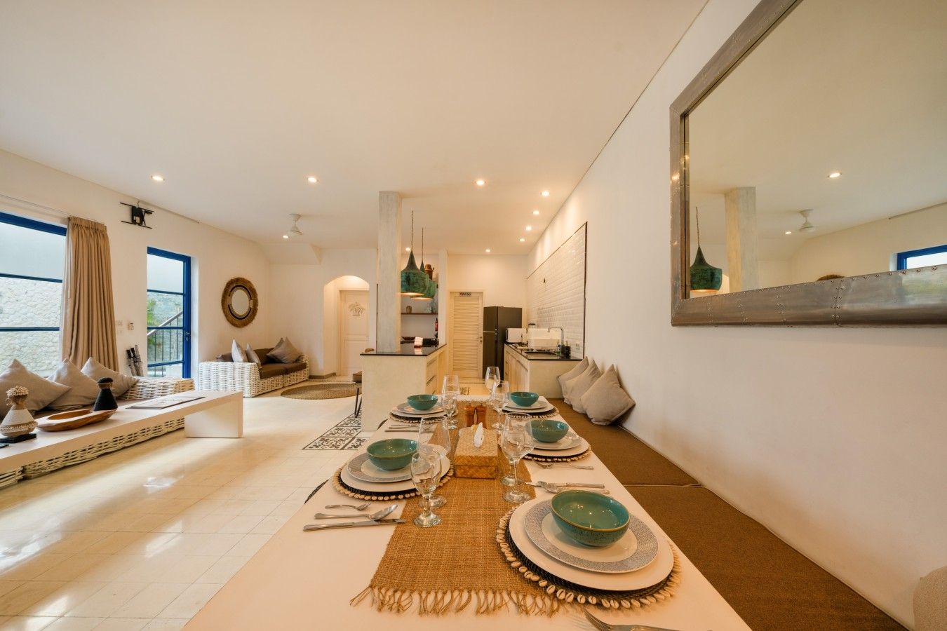 A dining area with a long table set for a meal, a kitchen in the background, and a living area with seating.