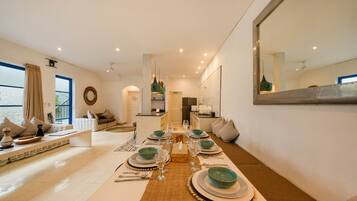 A dining area with a long table set for a meal, a kitchen in the background, and a living area with seating.