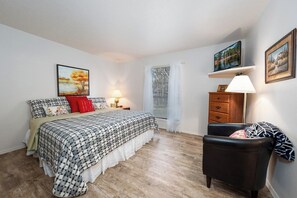 Une chambre à coucher comprenant un lit, une table de chevet, une lampe, une chaise et des œuvres d’art accrochées aux murs.