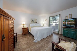 A bedroom with a bed, bedside tables, a dresser, a television, and a window with blinds.