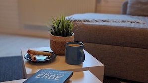 Una habitación acogedora con ventana, una mesita con un libro, una taza, una vela y una planta.