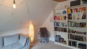 Une pièce chaleureuse avec un canapé gris, un fauteuil en osier, une bibliothèque remplie de livres et une lampe décorative.
