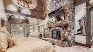 A spacious bedroom with a large bed, a stone fireplace, and a balcony with a view of trees. - Immaculate Golf Course Home, Private Hot Tub, Gym, Firepits (Beaver Creek)