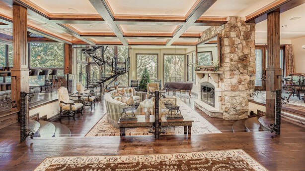 A spacious living area with a fireplace, a staircase, and a large window overlooking a forest. - Immaculate Golf Course Home, Private Hot Tub, Gym, Firepits (Beaver Creek)