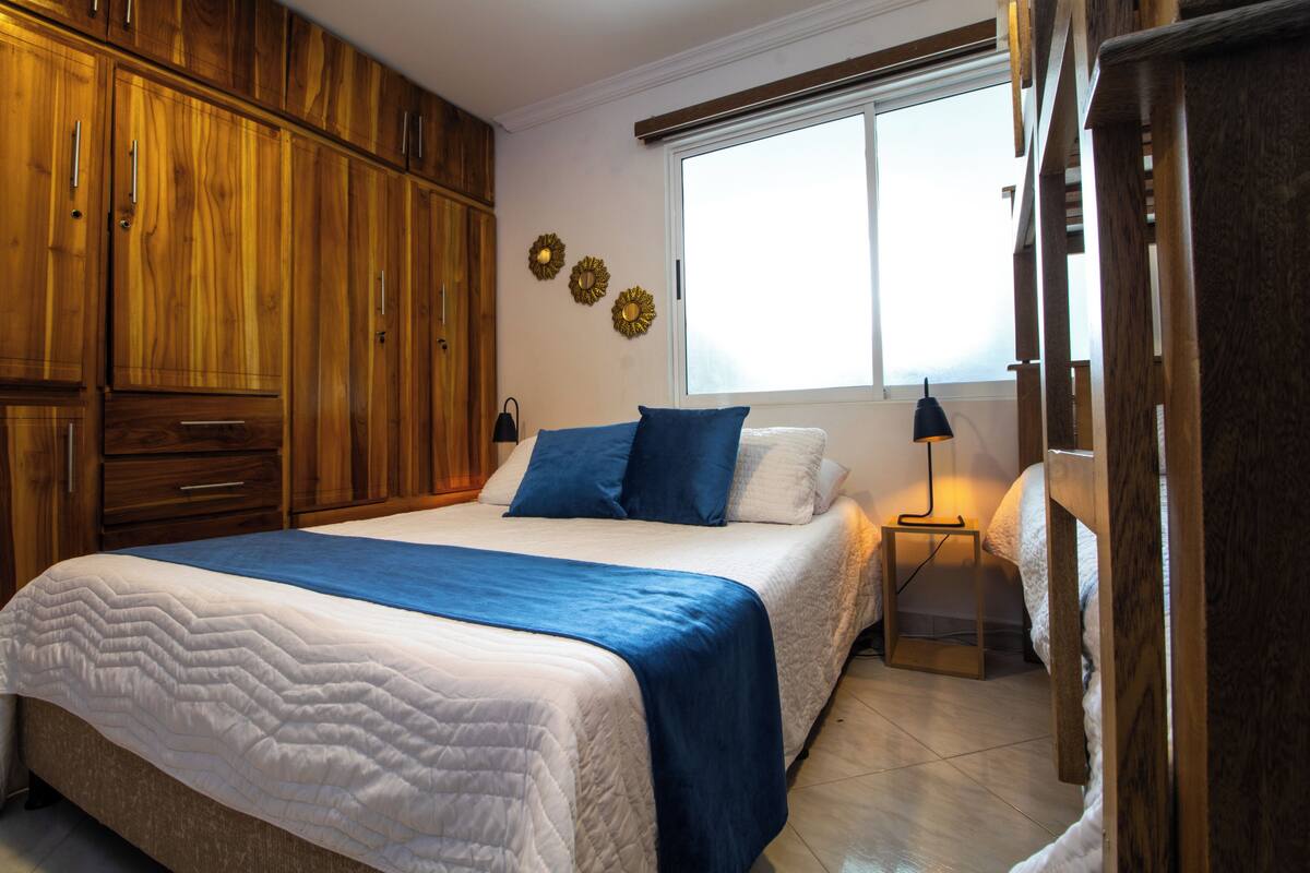 Un dormitorio con cama, armario de madera, lámparas de noche y una ventana.
