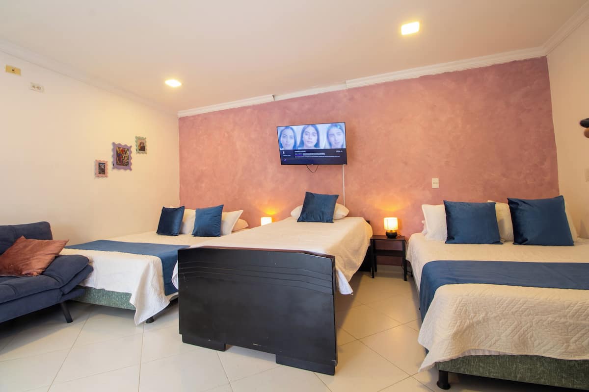 Una habitación de hotel con dos camas, un televisor montado en la pared y una mesita de noche con una lámpara.