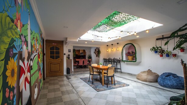 A dining area with a table and chairs, a ceiling skylight, and potted plants. - Kaobba Hostal (Medellín)