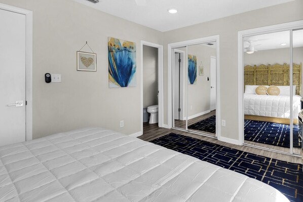 A bedroom with a large bed, a bathroom with a toilet and sink, and a mirrored closet with a bed and a decorative headboard.