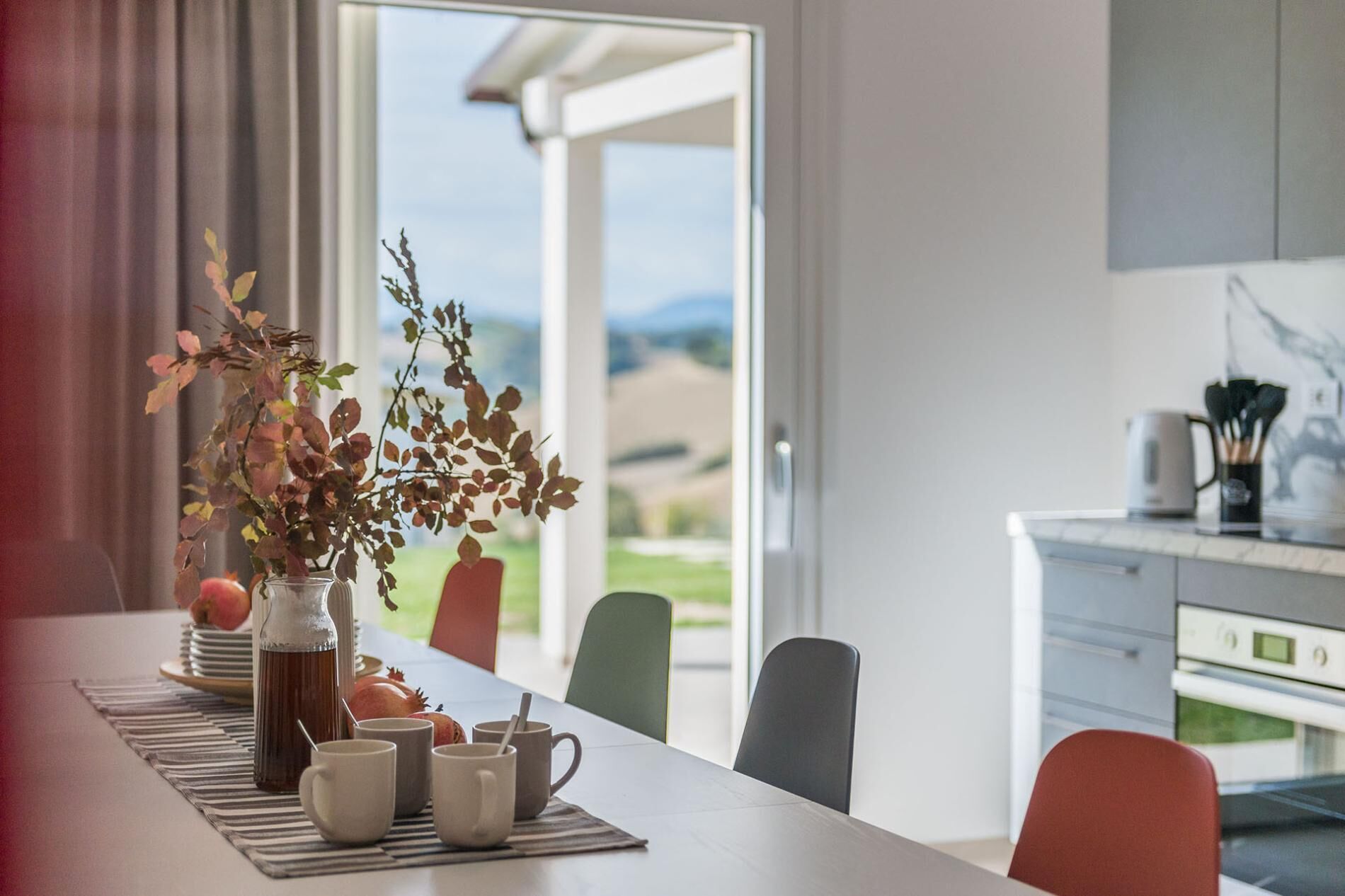 Ein Essbereich mit einem Tisch für vier Personen, einer Vase mit getrockneten Blumen und Blick ins Freie.