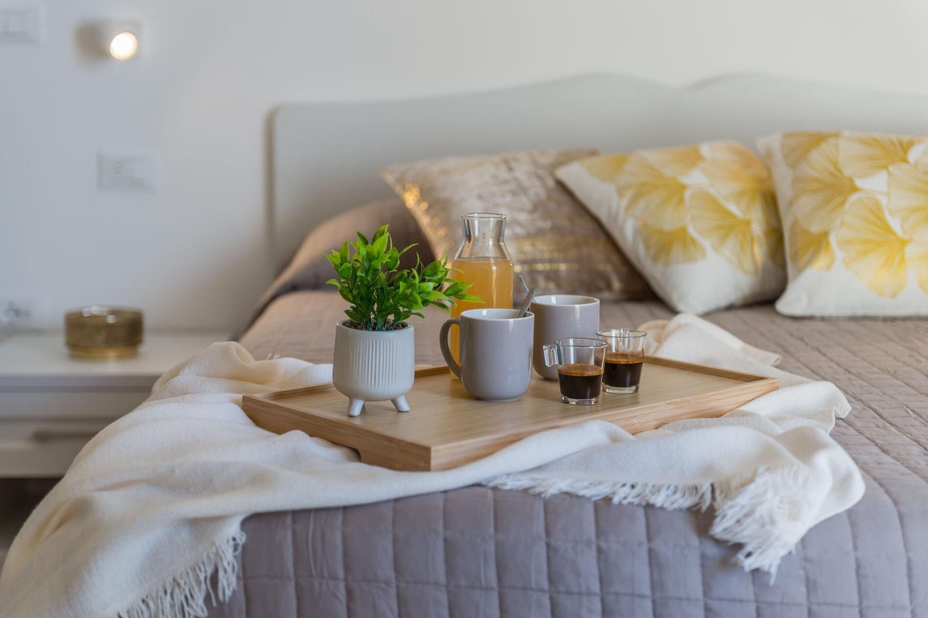 Una colazione ben presentata su un letto, con una pianta in vaso, un boccale e due tazze di caffè.