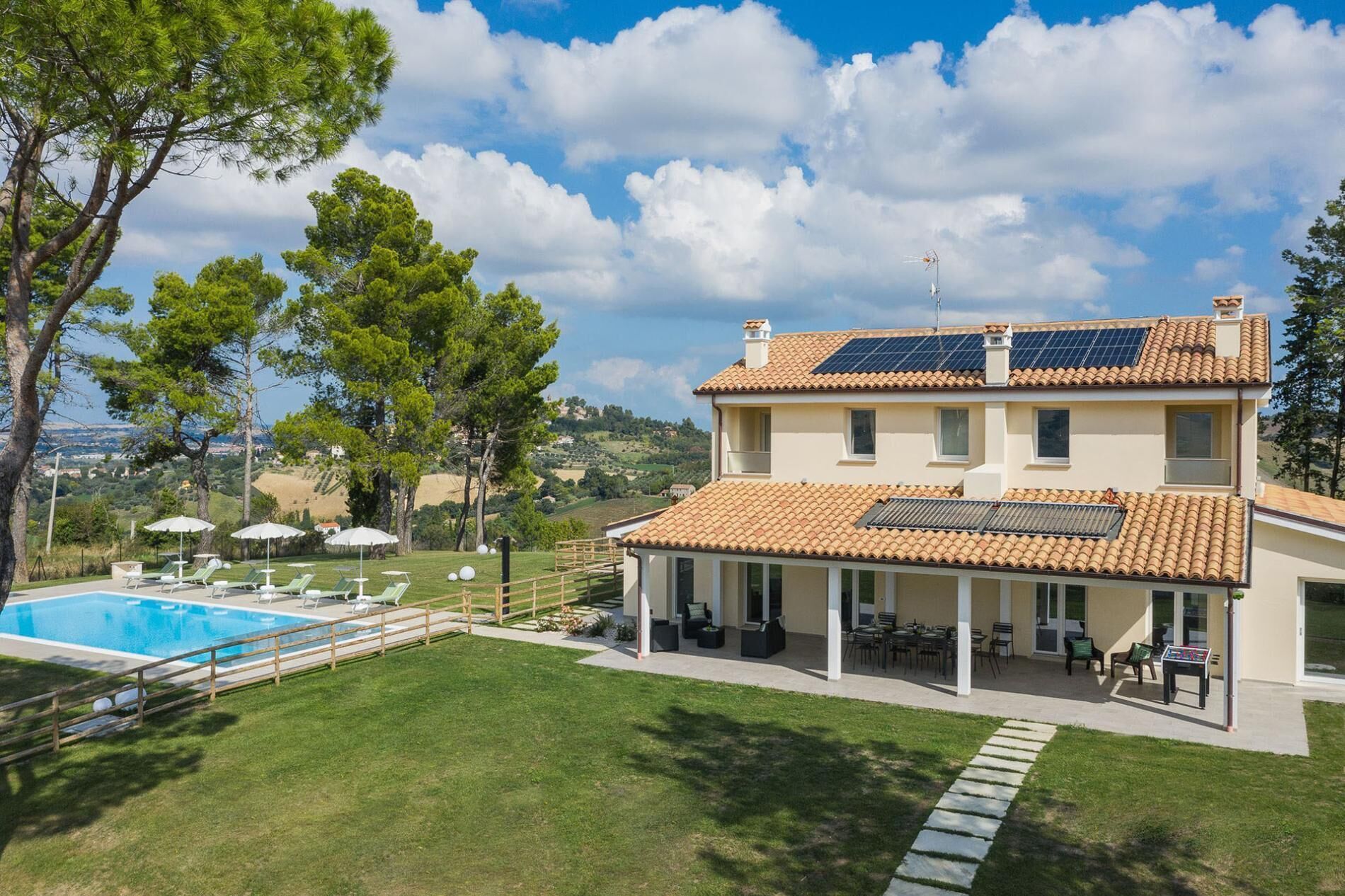 Una casa a due piani con piscina, area salotto esterna e pannelli solari sul tetto.