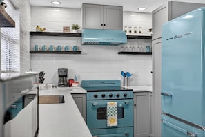 A kitchen with a teal stove, a refrigerator, and white tiled walls.