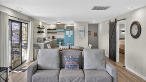Una sala de estar moderna con un sofá gris, una mesa de comedor y una cocina al fondo.