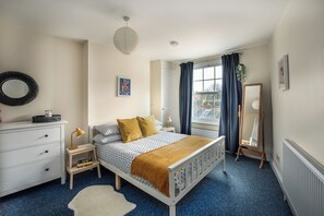 Een slaapkamer met een bed, een dressoir, nachtkastje, lamp en een grote spiegel.