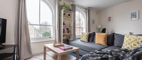 A modern living room with a sofa, a coffee table, a bookshelf, and a TV.