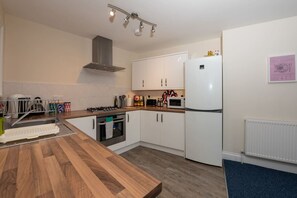 Een moderne keuken met witte kastjes, een houten aanrecht, een ingebouwde oven, een magnetron en een gasfornuis.