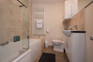 Een moderne badkamer met een douchecabine van glas, een witte badkuip, toilet en een wastafel met aanrechtblad.