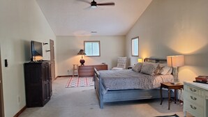 Een slaapkamer met een bed, dressoir, nachtkastje, lamp en een plafondventilator.