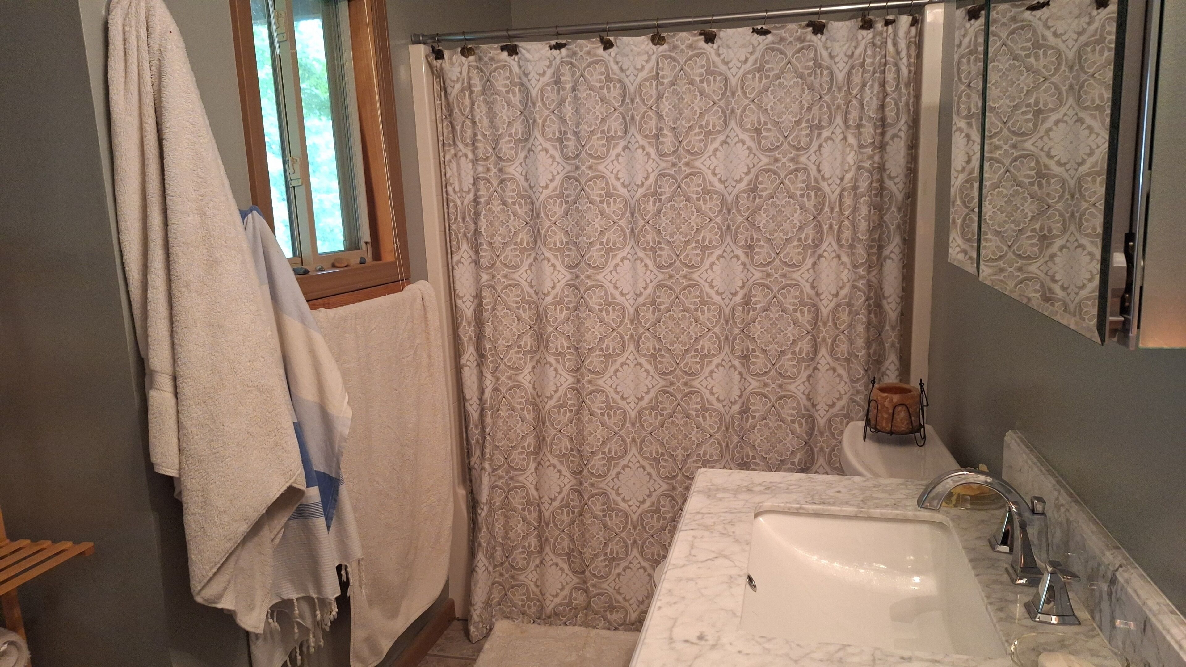 A bathroom with a white sink, a shower curtain with a floral pattern, and a wooden window frame.