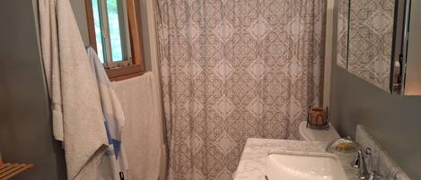 A bathroom with a white sink, a shower curtain with a floral pattern, and a wooden window frame.