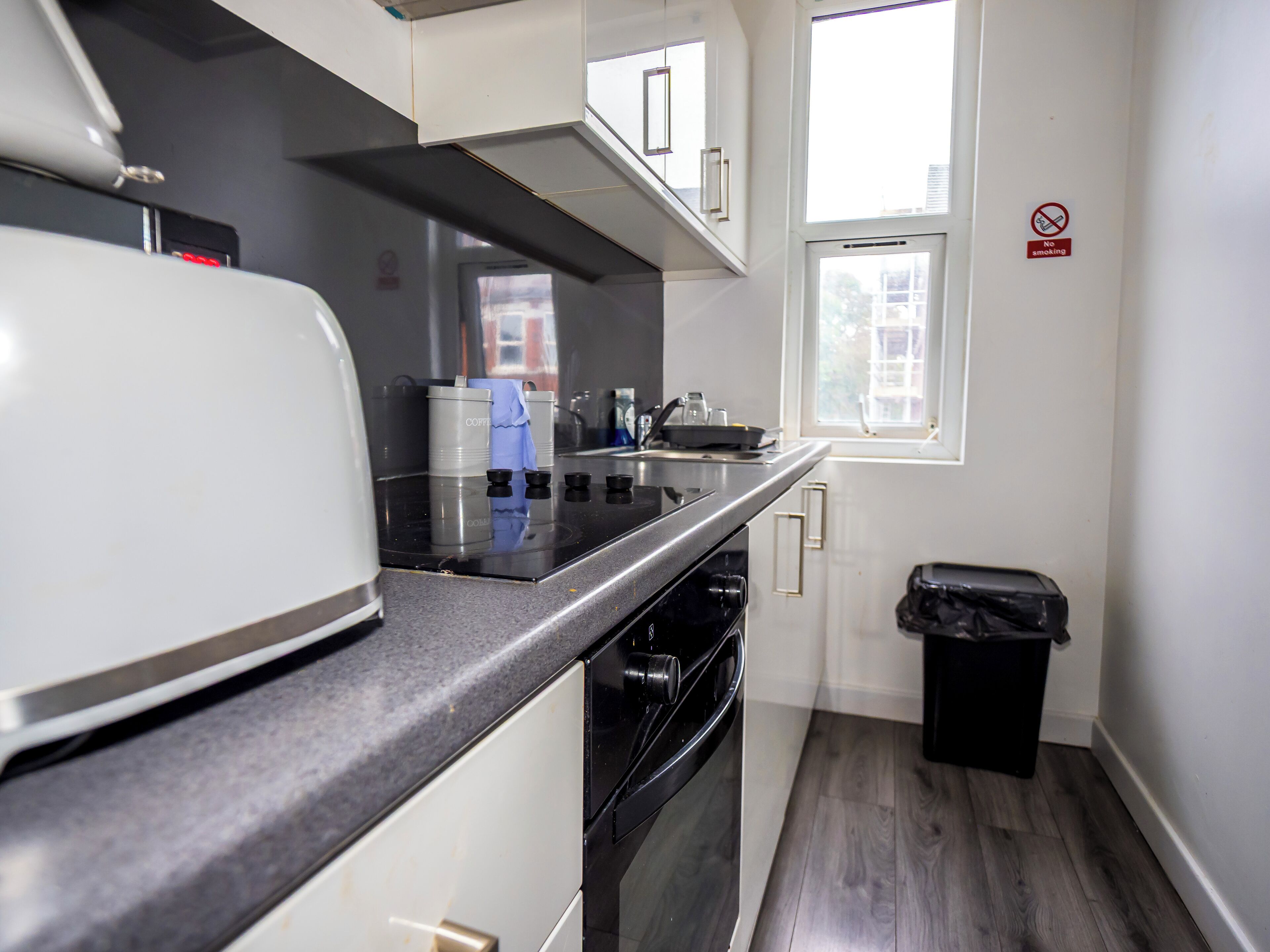 Una cocina compacta con microondas, estufa y pileta. Hay un cubo de basura y una ventana con vista.