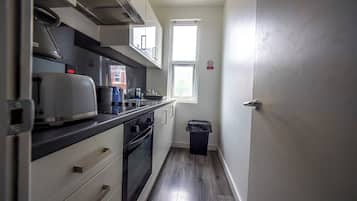 Eine kompakte Küche mit Mikrowelle, Toaster und Backofen. Ein Fenster bietet einen Ausblick und ein Mülleimer ist vorhanden.