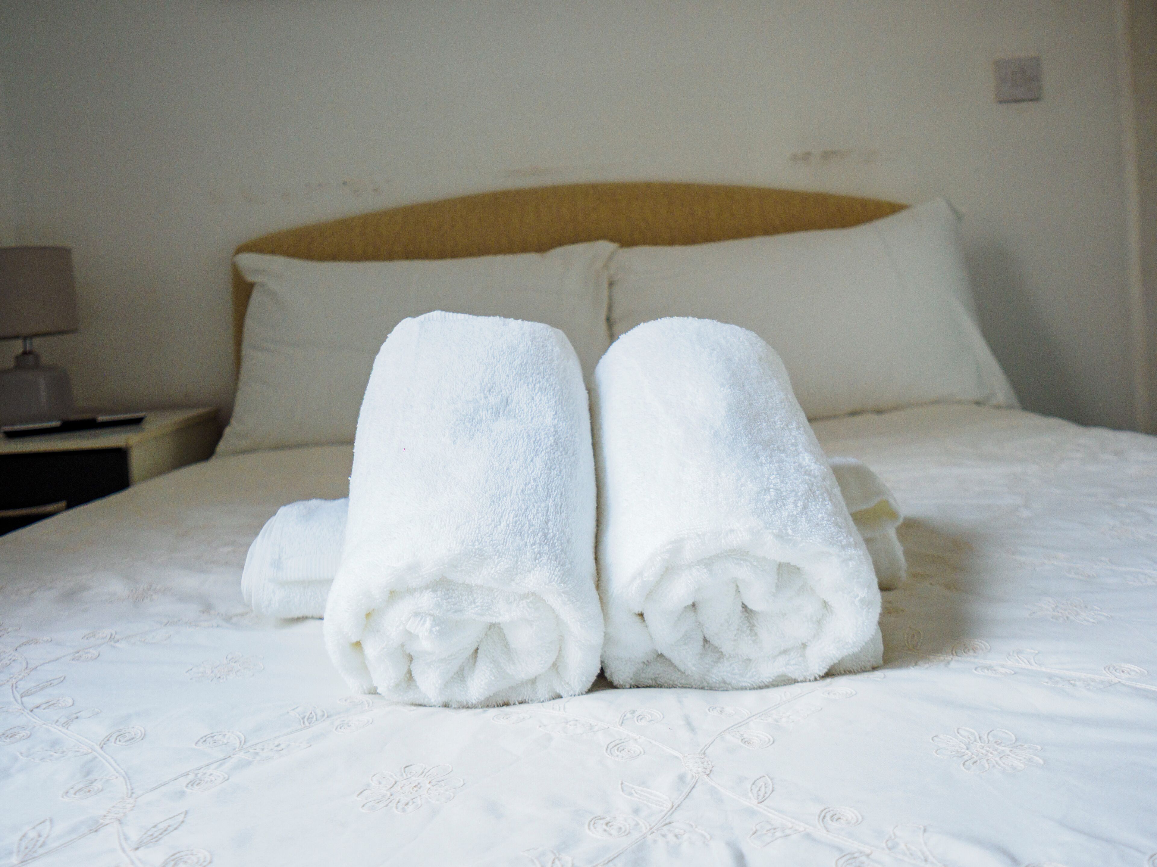 A neatly made bed with two rolled towels placed on the bed.