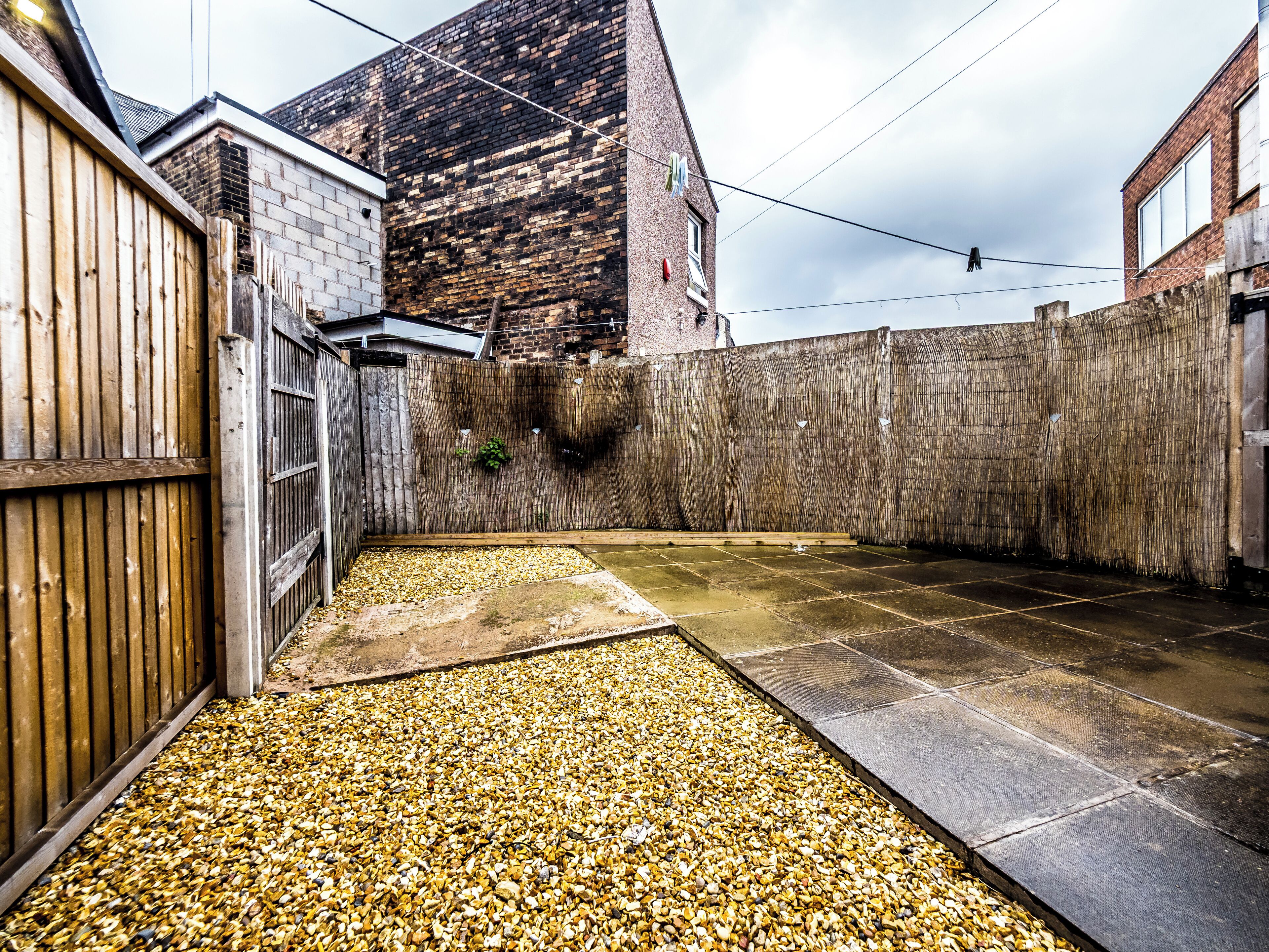 A courtyard with a gravel path, a wooden fence, and a brick wall.