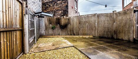 A courtyard with a gravel path, a wooden fence, and a brick wall.
