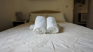 A hotel room with a bed, pillows, a nightstand, a lamp, and a painting of a city skyline. - Ensuite1 Woodhouse private bath 2kitchen (Stoke-on-Trent)