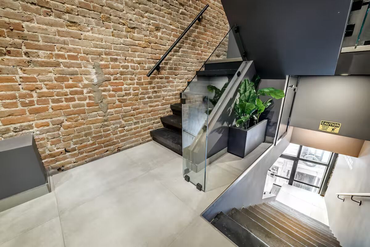 A staircase with a glass railing, a brick wall, and a caution sign.