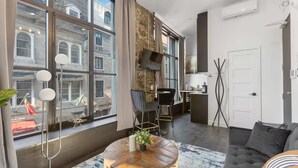 A modern living room with large windows, a round wooden coffee table, a black sofa, and a dining area with a table and chairs. - AirStay-Saint Paul  (Montréal)