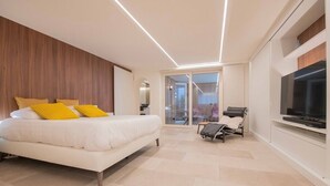 Een moderne slaapkamer met een groot bed, een televisie en een glazen deur naar een balkon.