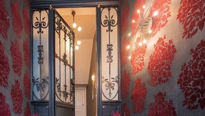 Een trap die leidt naar een kamer met een behang waarop een bloemenpatroon is afgebeeld en een zwart metalen hekwerk.