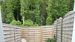 A round wooden table with four chairs, surrounded by a wooden fence and gravel ground.